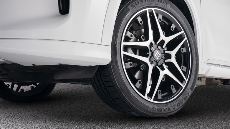 Muestra de neumático con rines de lujo delanteros de camioneta SUV hibrida enchufable DFSK E5 color blanca.