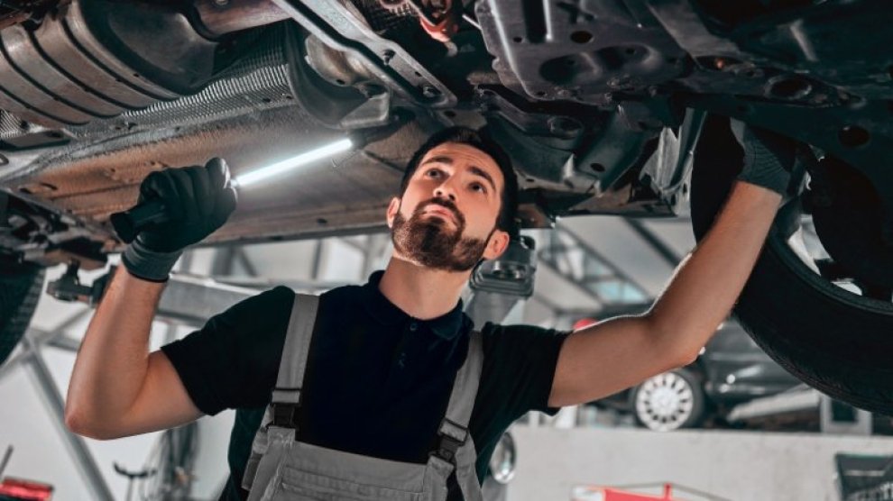 <p>Técnico especializado revisando el estado de un auto por la parte de abajo con una linterna en su mano.</p>